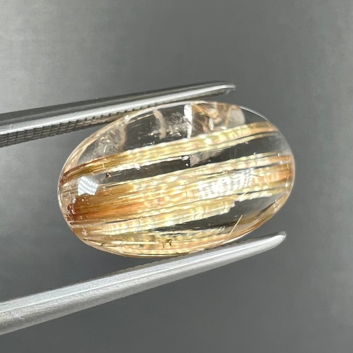 A loose, oval cabochon cut cat's eye golden rutilated quartz stone.