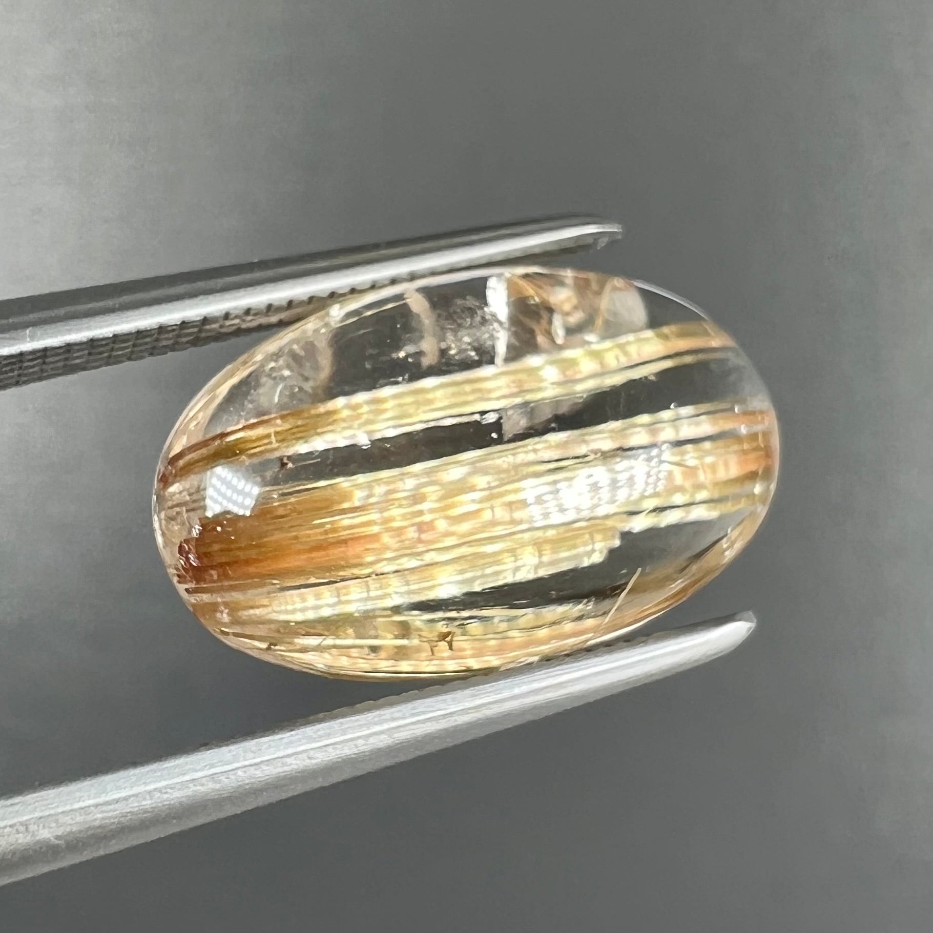 A loose, oval cabochon cut cat's eye golden rutilated quartz stone.