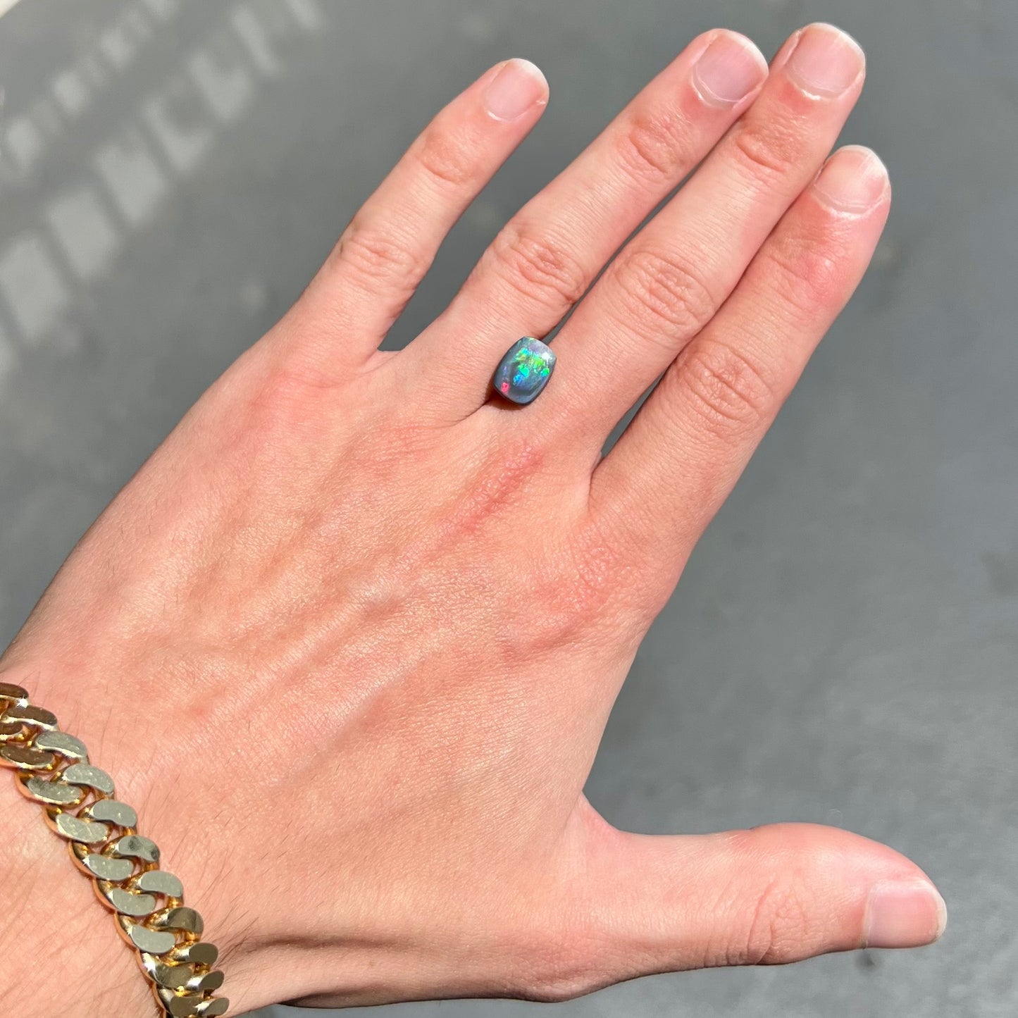 A loose, cushion cabochon cut semi-black opal stone. The stone plays multiple colors.
