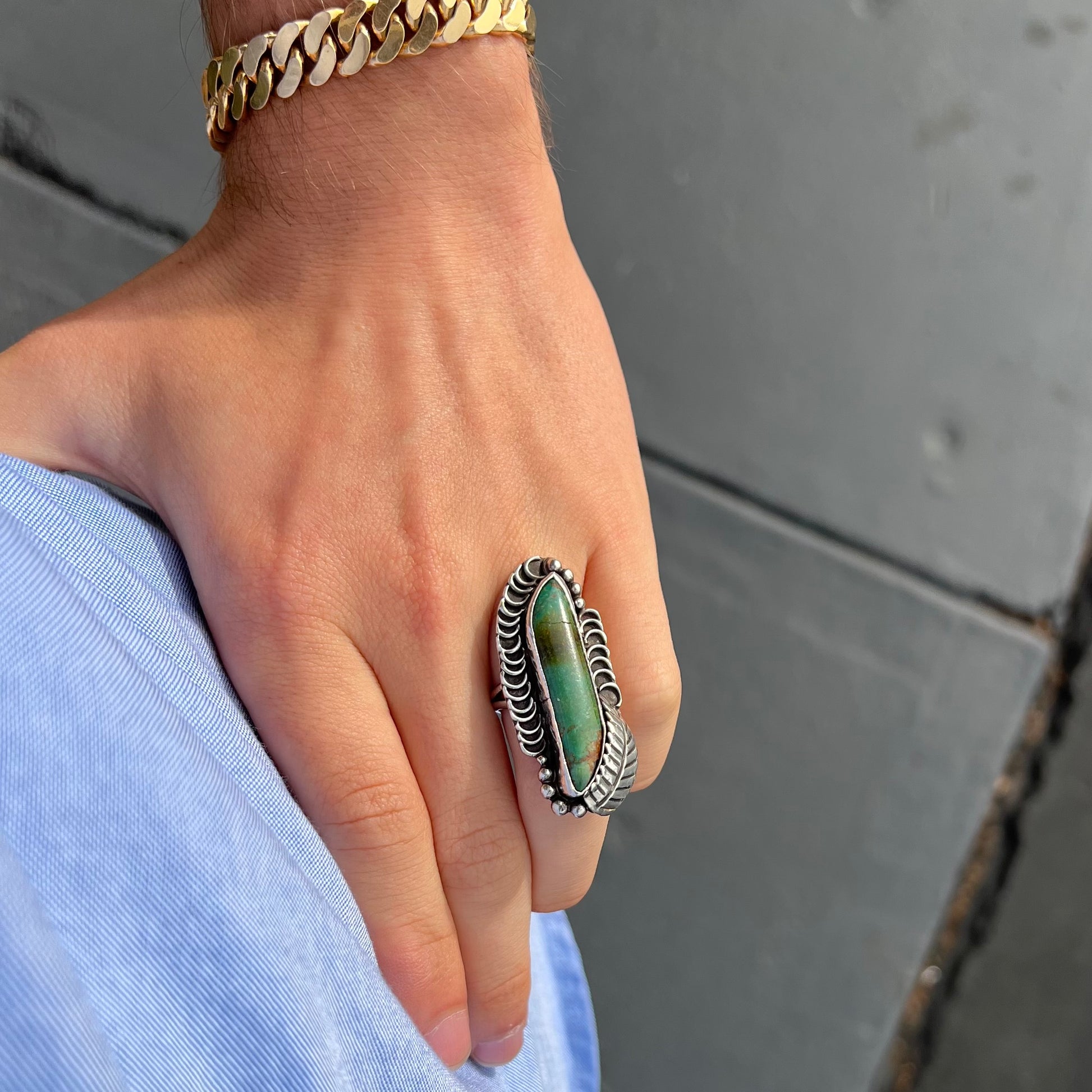 A sterling silver Navajo style ring set with a turquoise stone that shows colors of green, yellow, and reddish brown.