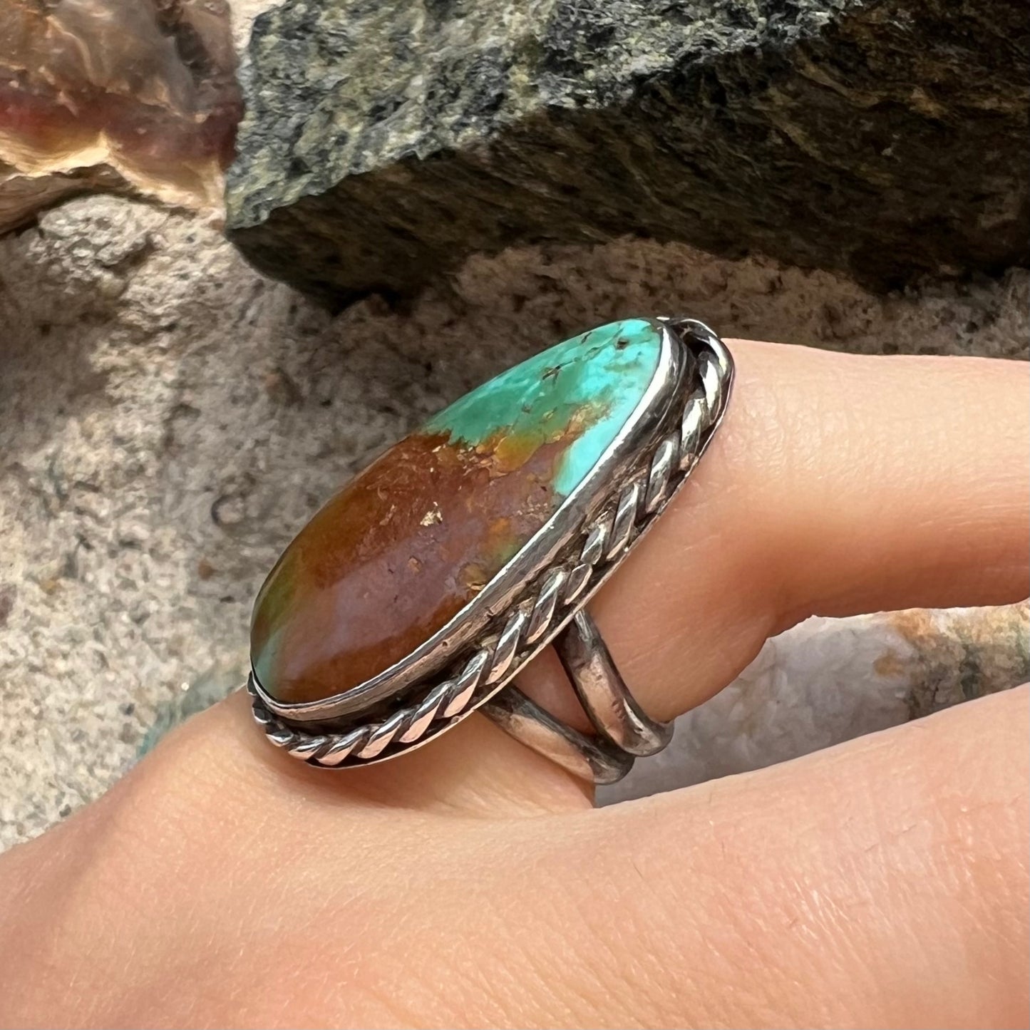 A sterling silver ring made with a rope bezel design and set with a green and brown Royston turquoise stone.