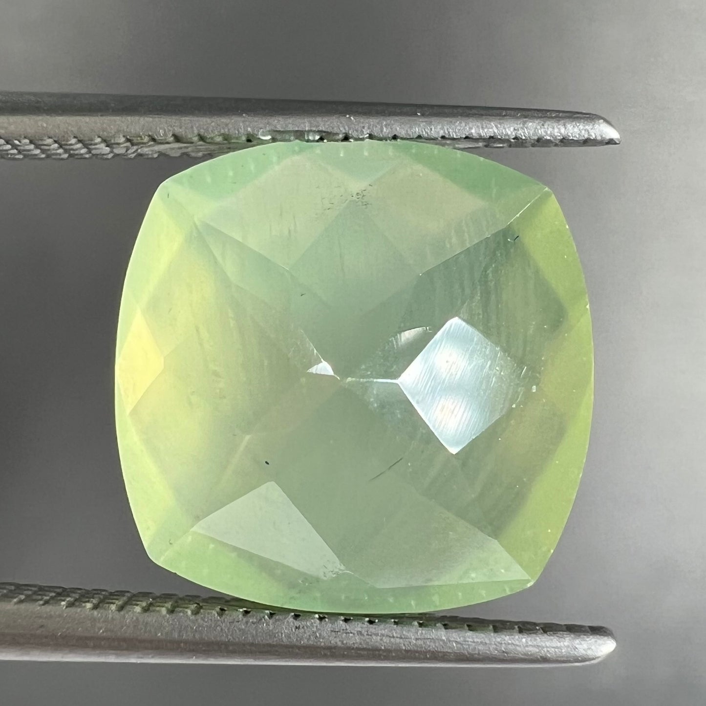 A loose, checkerboard cushion cut prehnite gemstone. The stone is a sleepy yellow green color.
