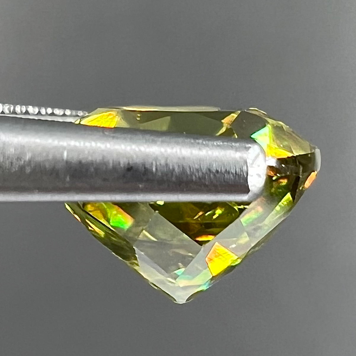 A loose, round brilliant cut sphene gemstone. The stone is green with orange, green, blue, and yellow flashes.