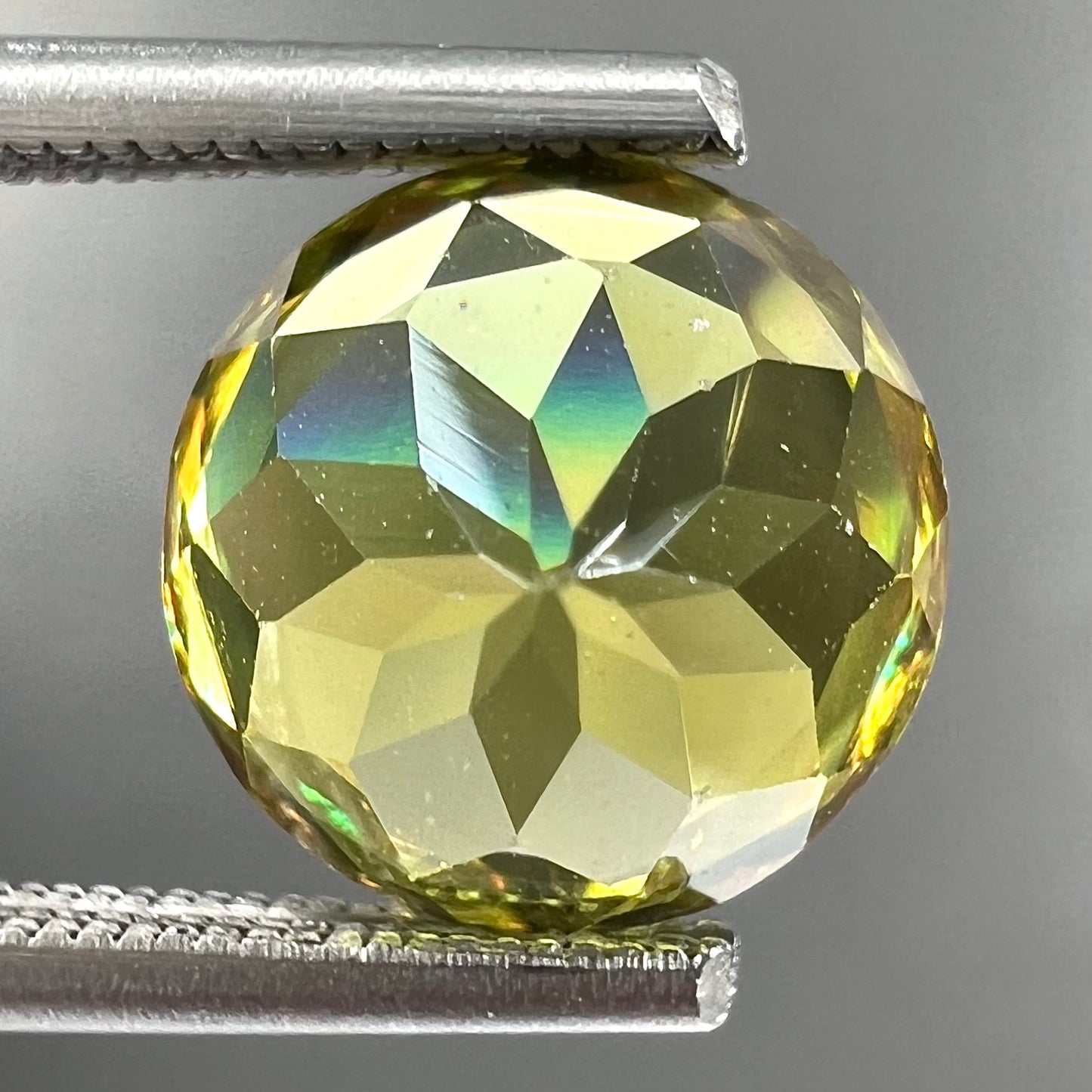 A loose, round brilliant cut sphene gemstone. The stone is green with orange, green, blue, and yellow flashes.