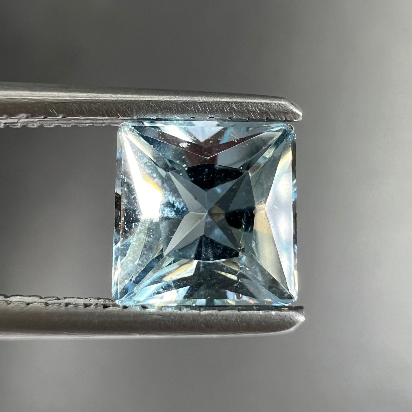 A loose, princess cut aquamarine gemstone. The stone is a light blue color.
