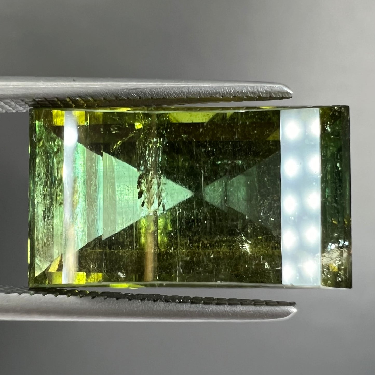 A rectangular step-cut yellowish green tourmaline gemstone.