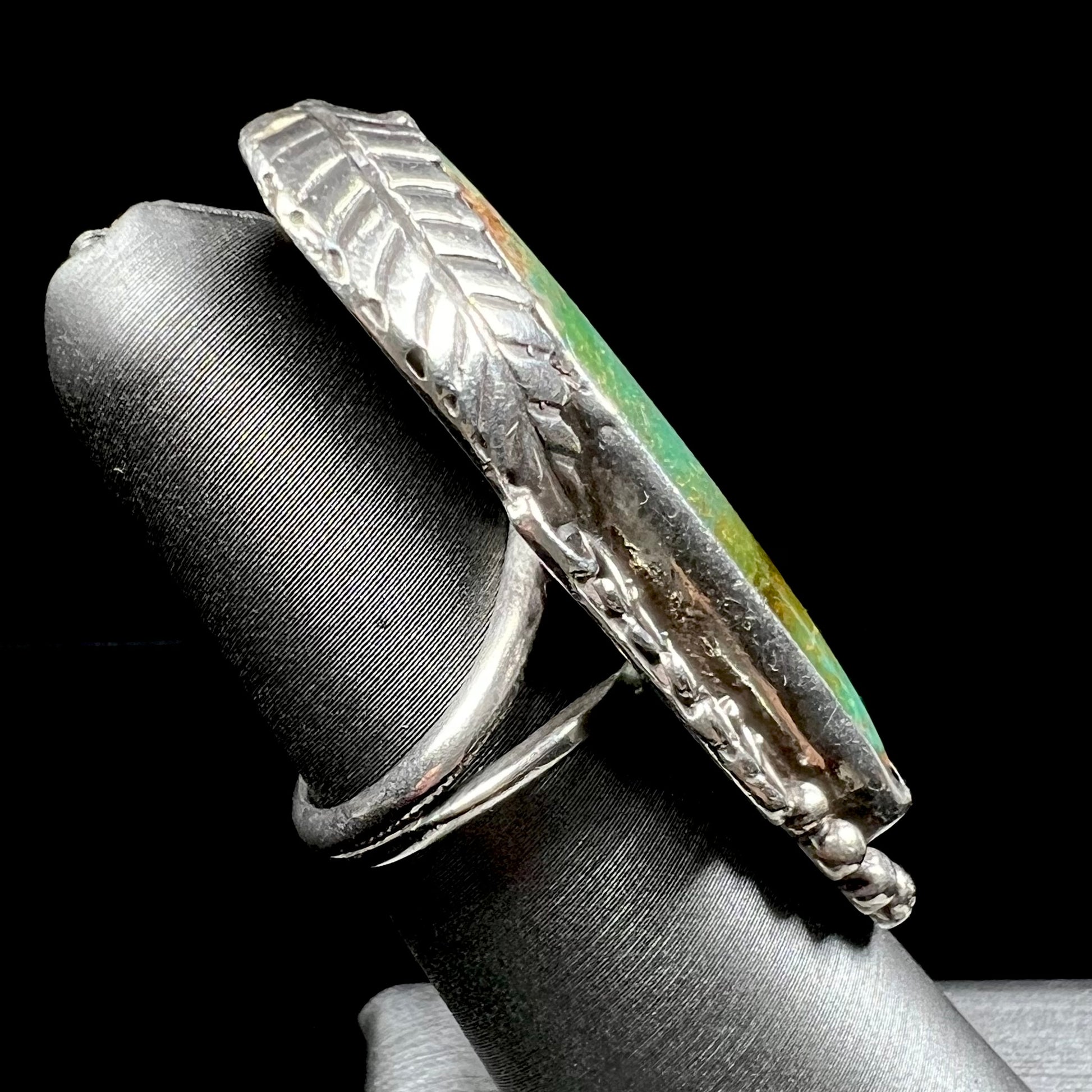A sterling silver Navajo style ring set with a turquoise stone that shows colors of green, yellow, and reddish brown.