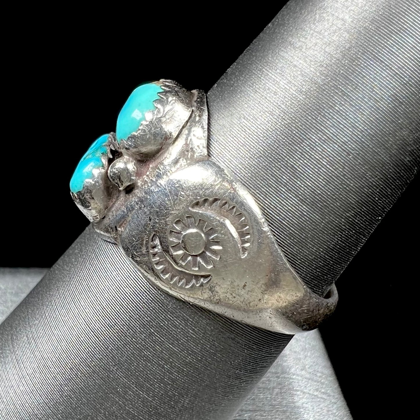 A unisex sterling silver ring bezel set with two Pilot Mountain turquoise stones.  The ring is stamped with sun patterns.