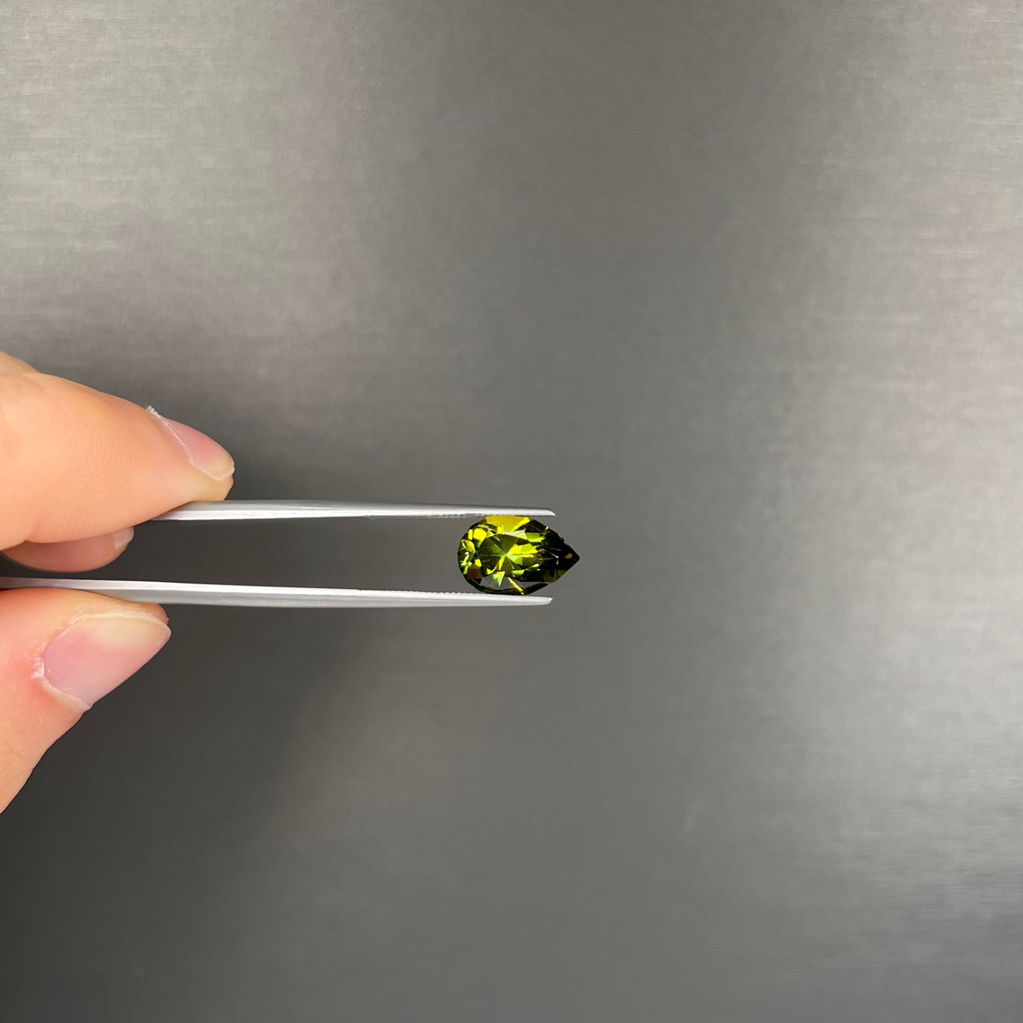 A loose, pear shaped green tourmaline gemstone. The color is dark green with a yellow secondary hue.