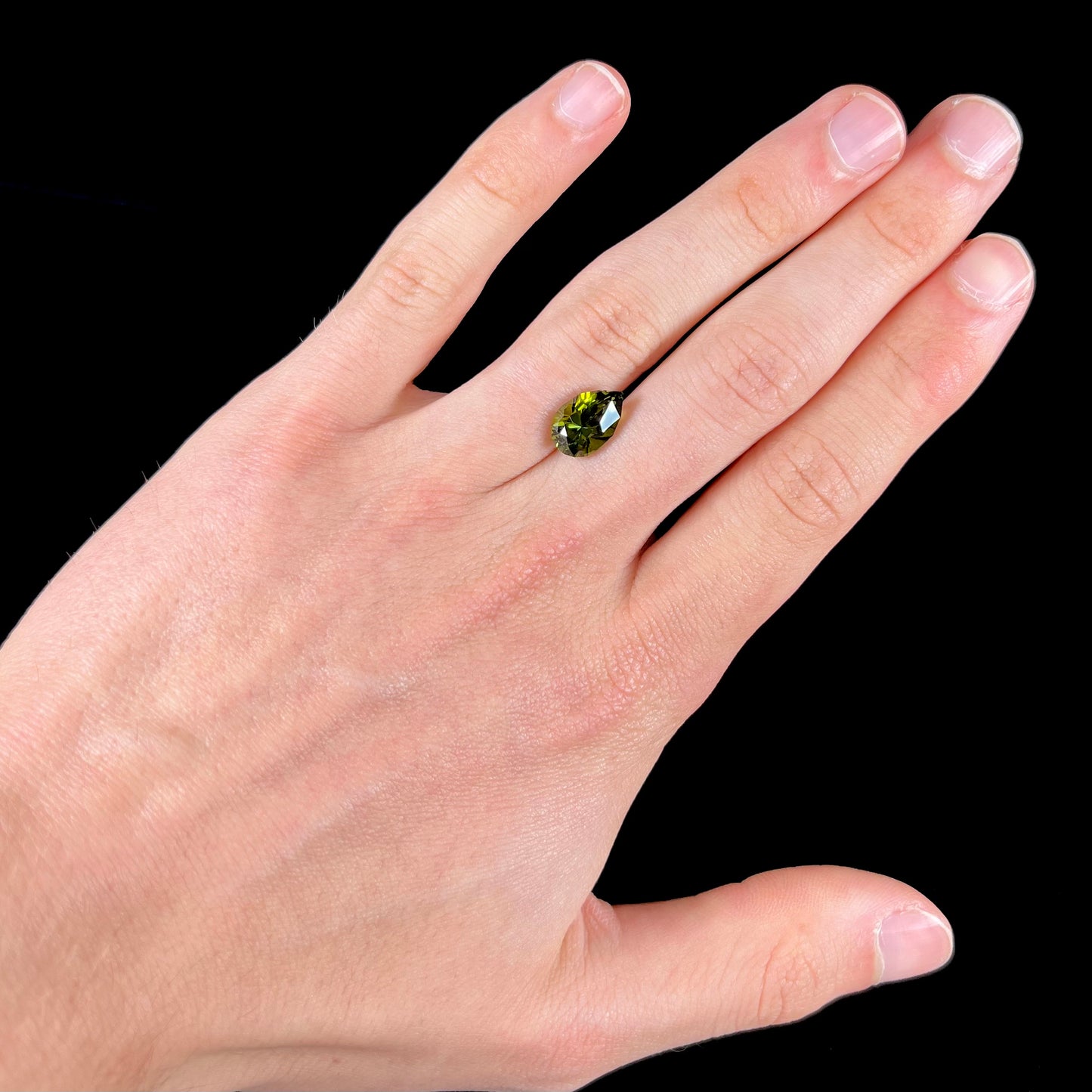 A loose, pear shaped green tourmaline gemstone. The color is dark green with a yellow secondary hue.