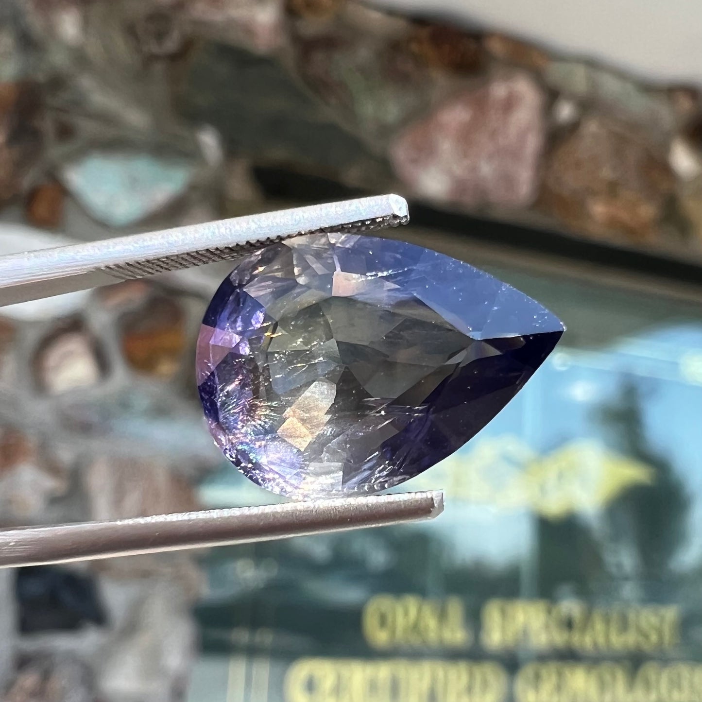 A loose, pear shaped bicolor iolite gemstone. The stone shows violite purple and silver colors.