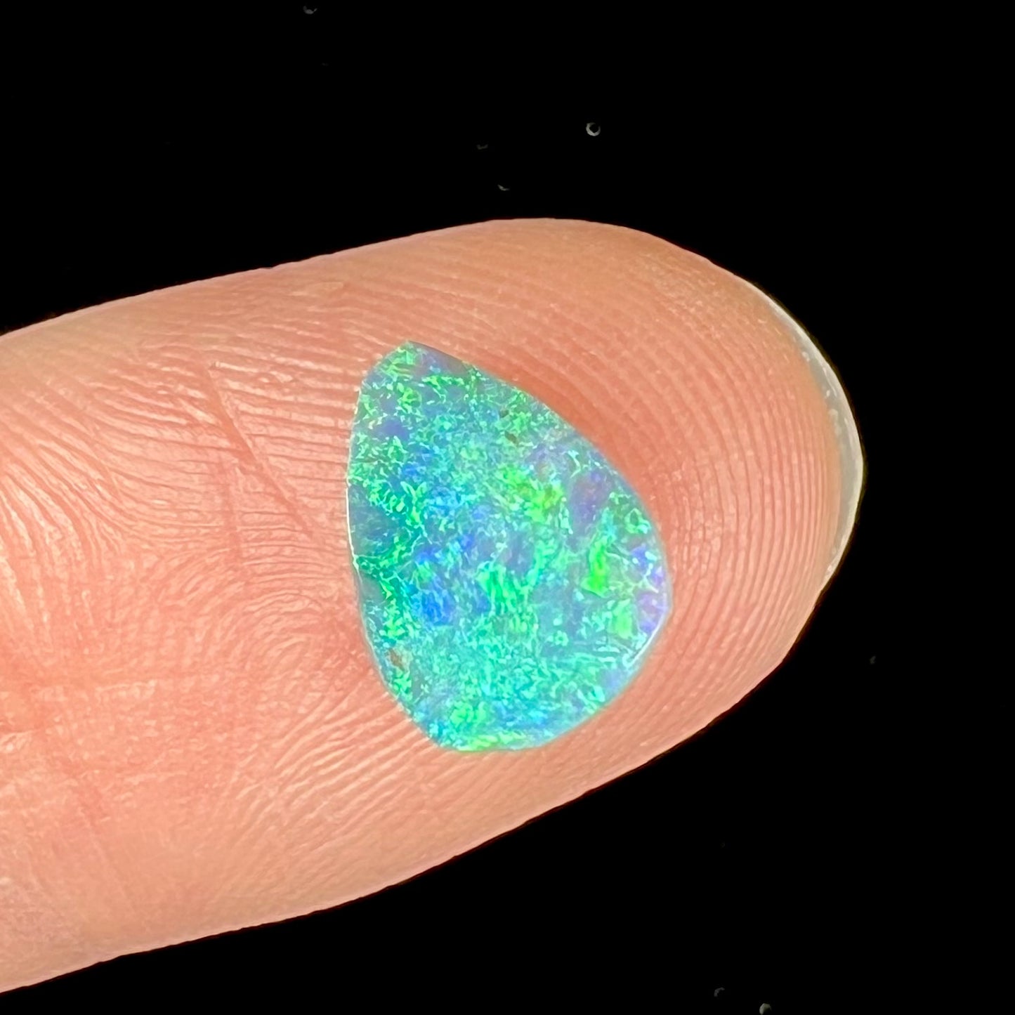 A loose, pear shaped black opal from LIghtning Ridge, Australia. The opal shines blue and green colors.