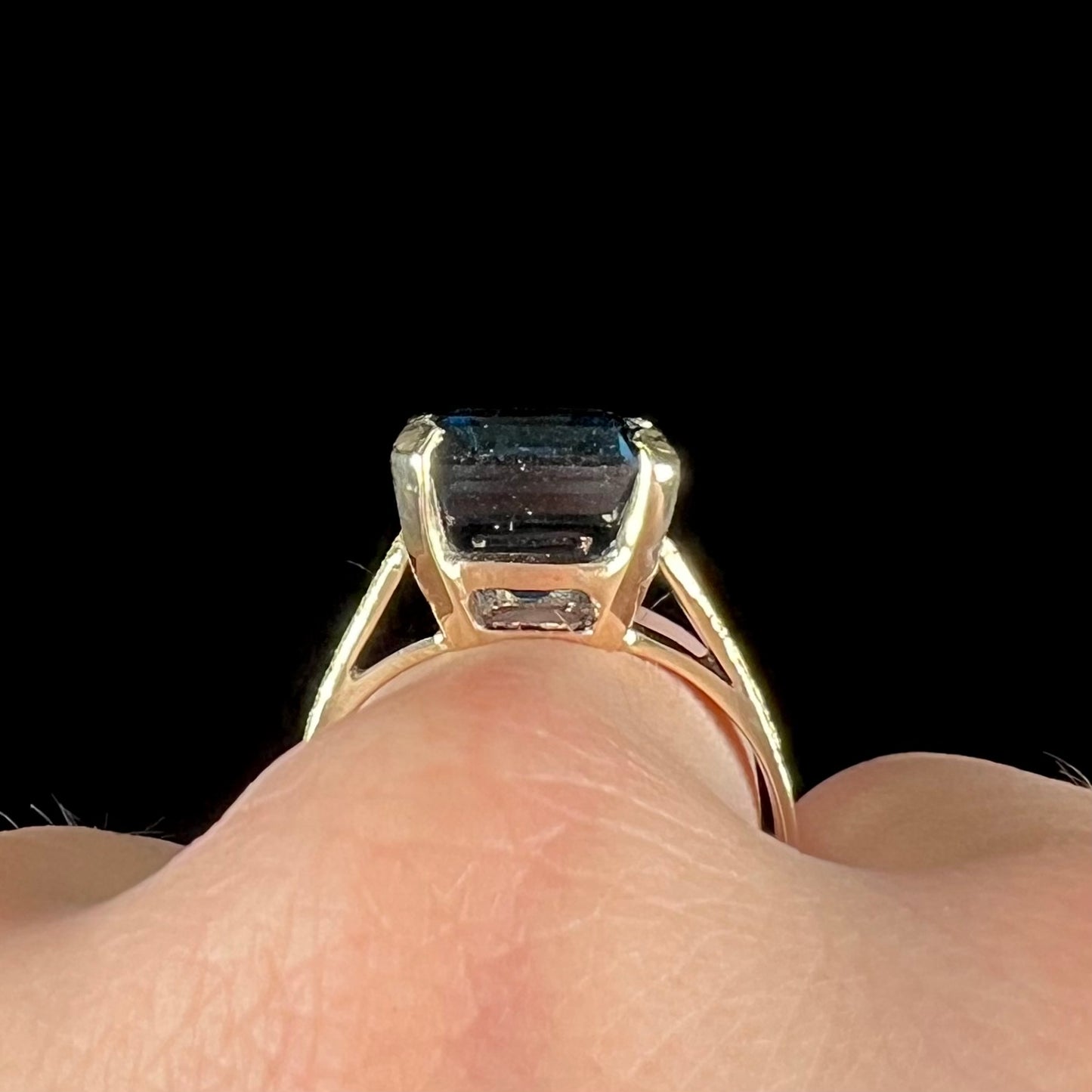 A ladies' yellow gold London blue topaz solitaire ring. The ring is textured, and the topaz is emerald cut.
