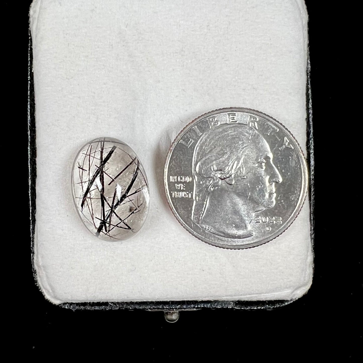 A loose, oval cabochon cut clear quartz stone with black tourmaline needle inclusions.