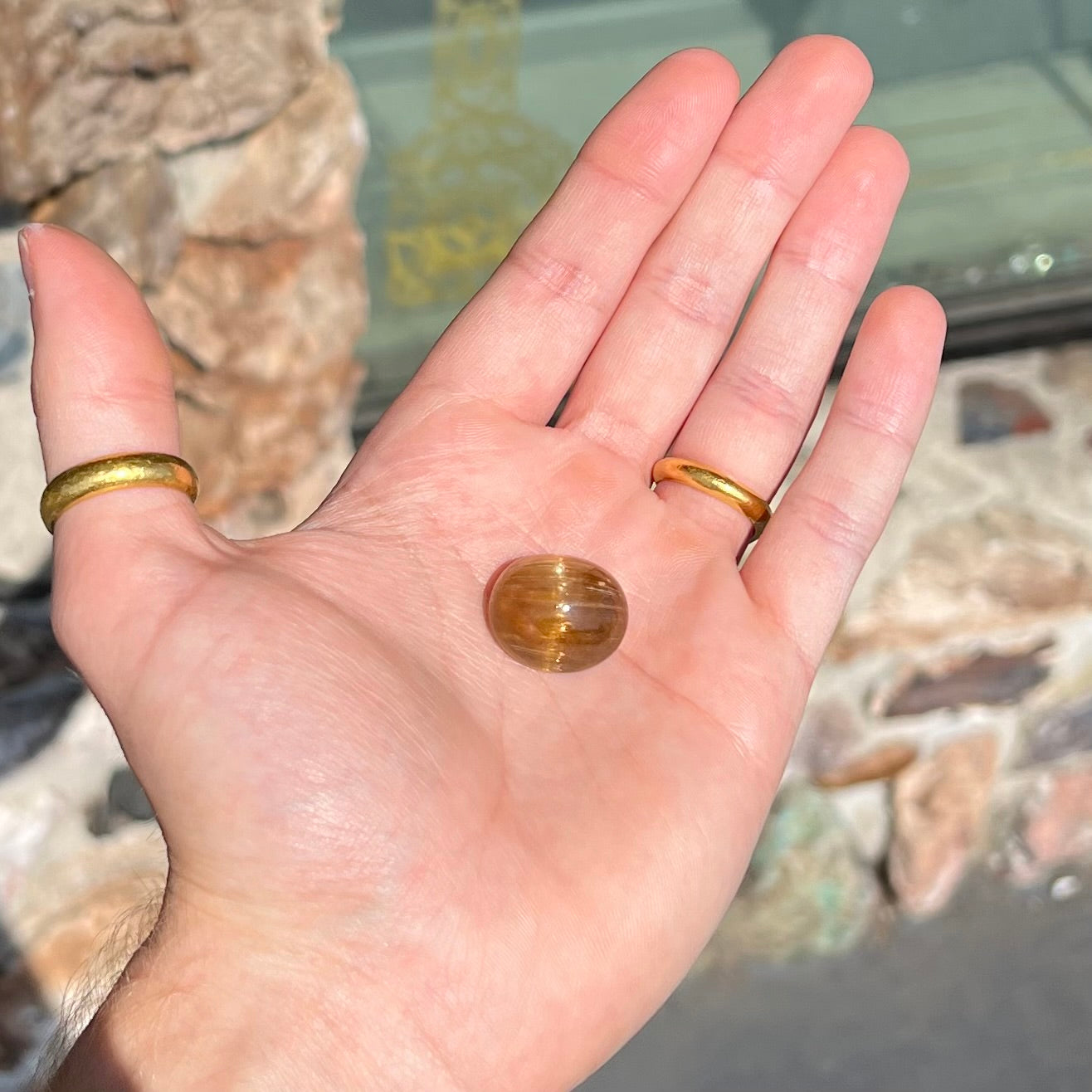A loose, golden brown cat's eye dravite tourmaline gemstone. The stone is cut into an oval shaped cabochon.