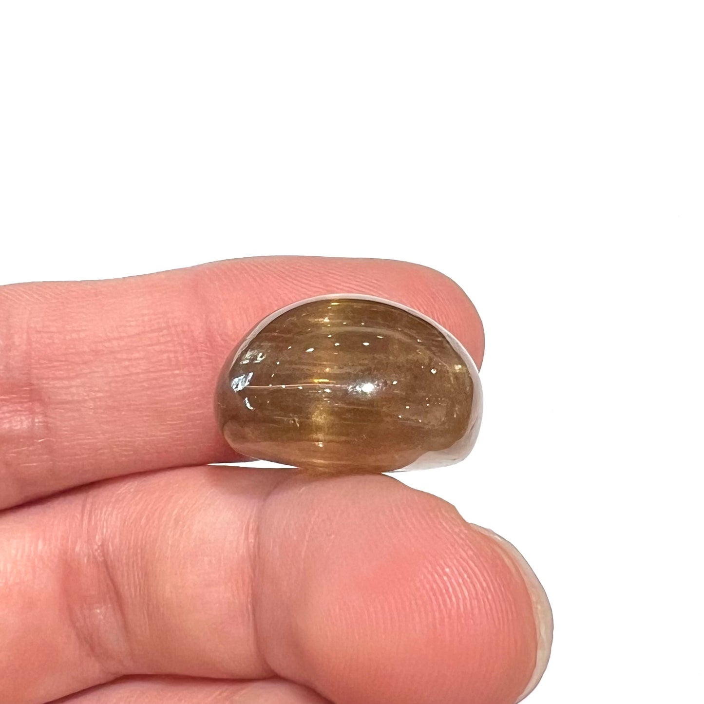 A loose, golden brown cat's eye dravite tourmaline gemstone. The stone is cut into an oval shaped cabochon.
