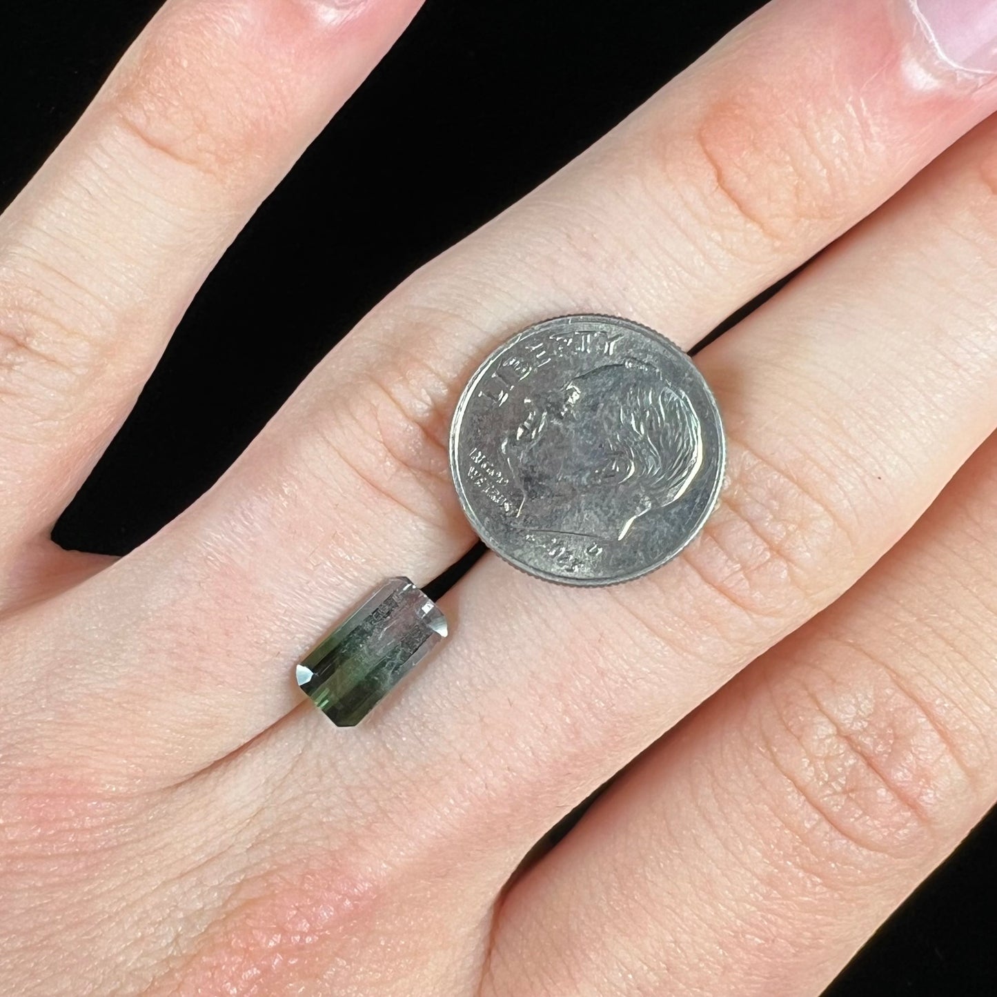 A loose, emerald cut tricolor tourmaline gemstone. The stone transitions from green to blue to white colors.