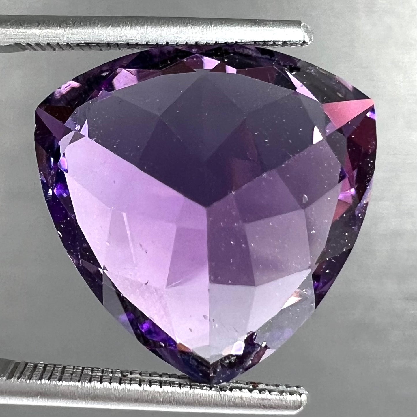 A loose, faceted trillion cut amethyst gemstone.