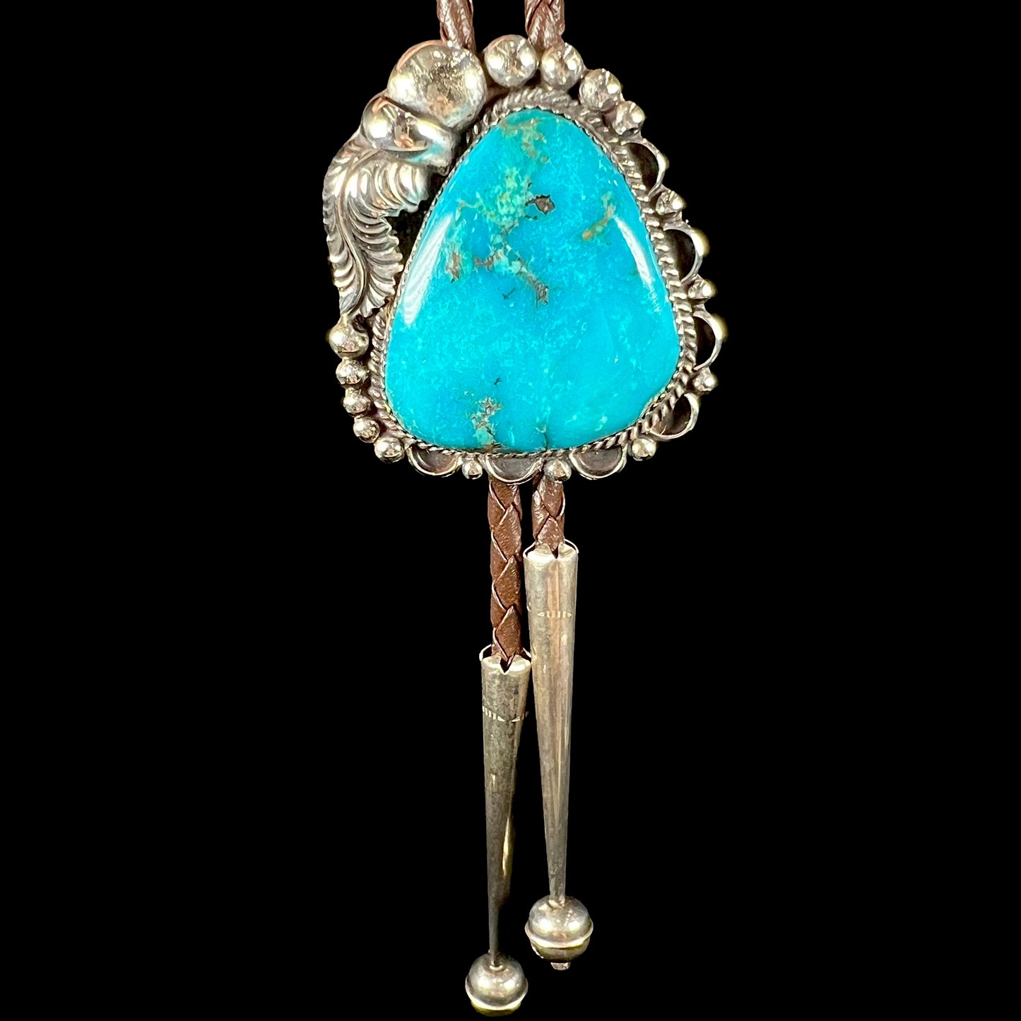 A men's sterling silver, Navajo style bolo tie set with a Pilot Mountain turquoise stone.  The rope is brown leather.