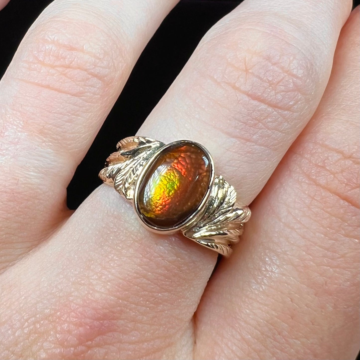 A unisex oval cabochon cut fire agate ring cast in yellow gold. The stone flashes green and red colors.