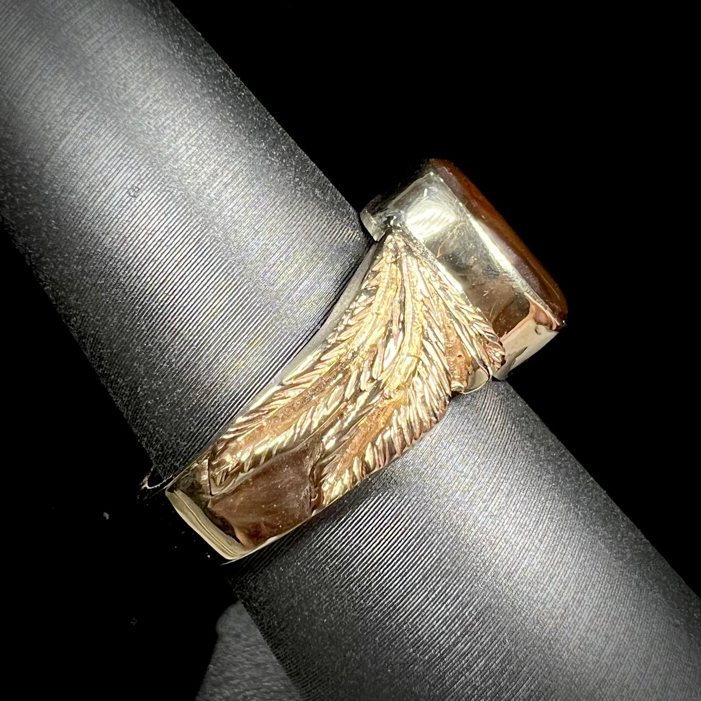 A unisex oval cabochon cut fire agate ring cast in yellow gold. The stone flashes green and red colors.