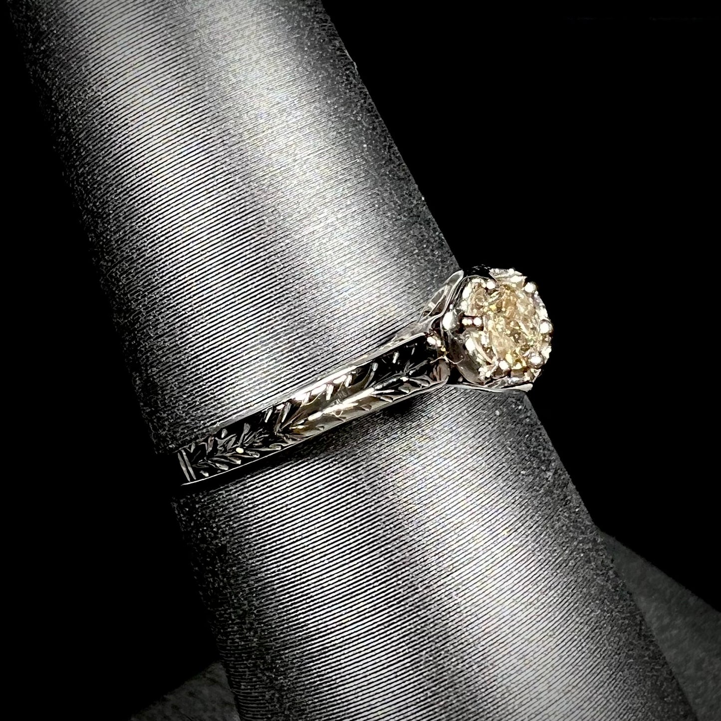 An Art Deco style 18 karat white gold diamond solitaire ring. The ring has scroll work on the side of the shank.