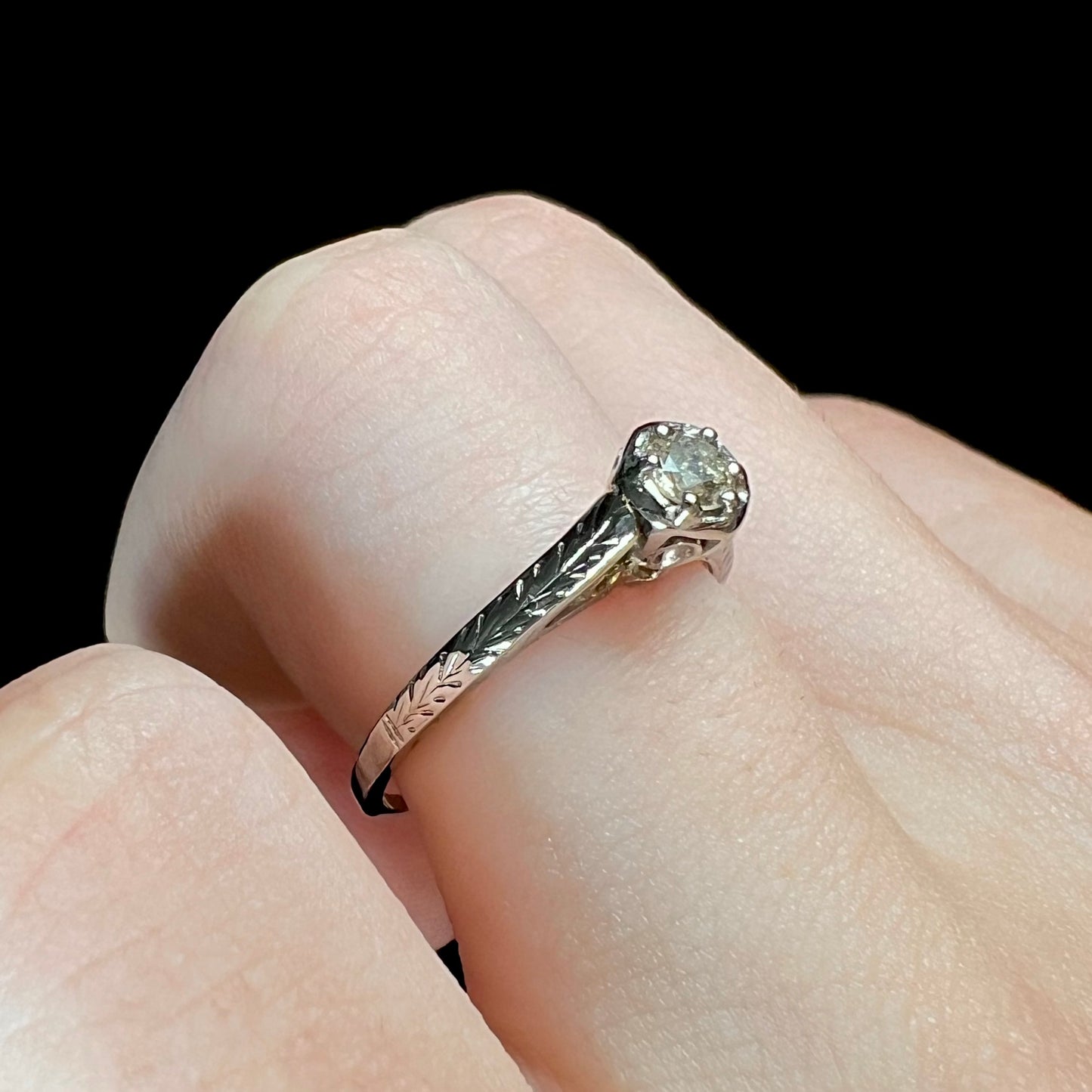 An Art Deco style 18 karat white gold diamond solitaire ring. The ring has scroll work on the side of the shank.