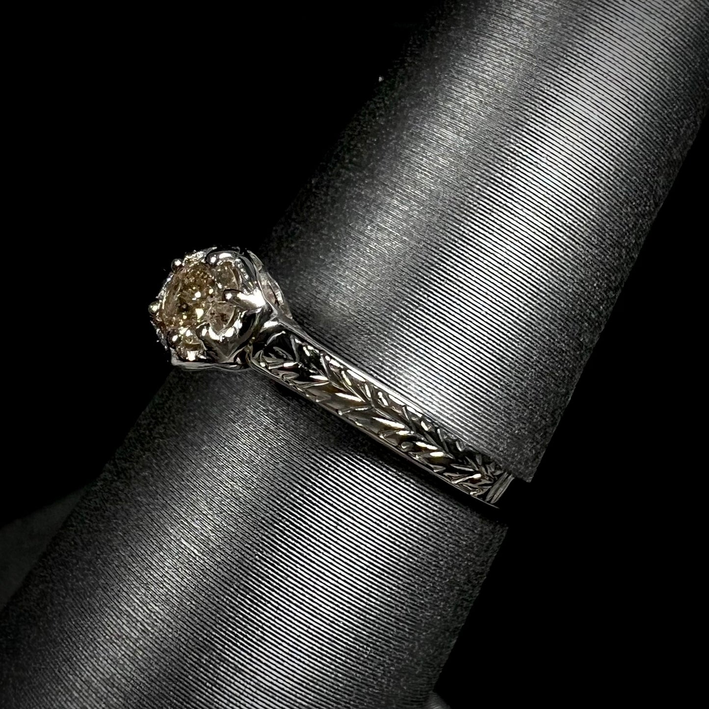An Art Deco style 18 karat white gold diamond solitaire ring. The ring has scroll work on the side of the shank.