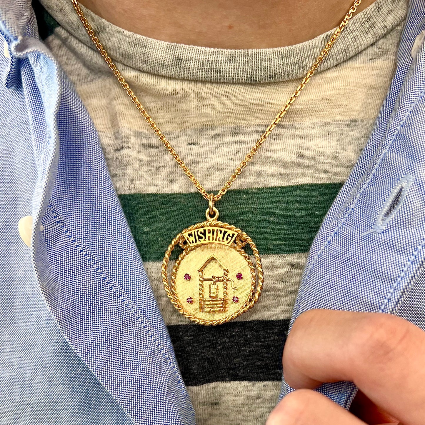 A yellow gold pendant depicting a picture of a wishing well, set with four natural rubies. The word "WISHING" sits at the top of the pendant.