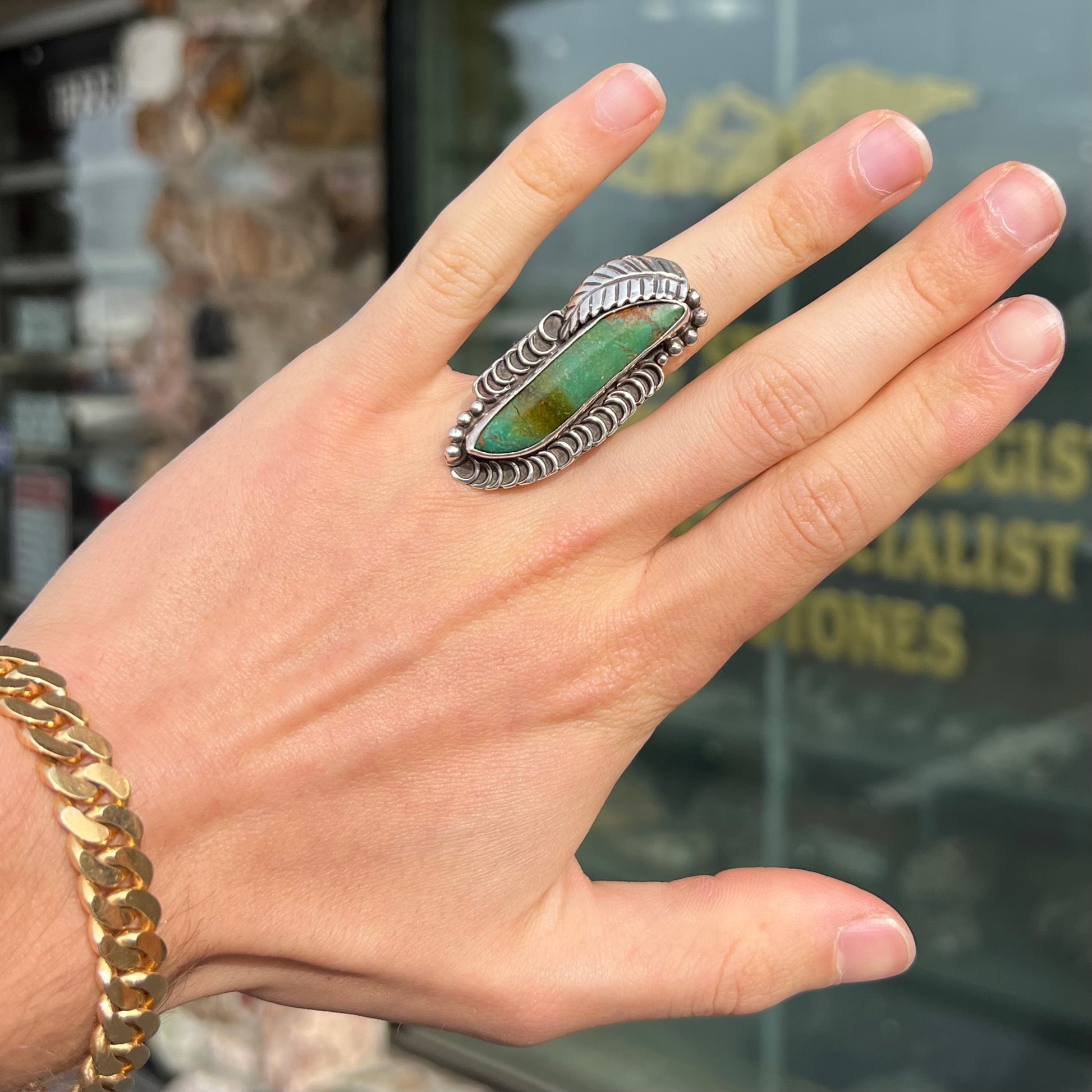 A sterling silver Navajo style ring set with a turquoise stone that shows colors of green, yellow, and reddish brown.