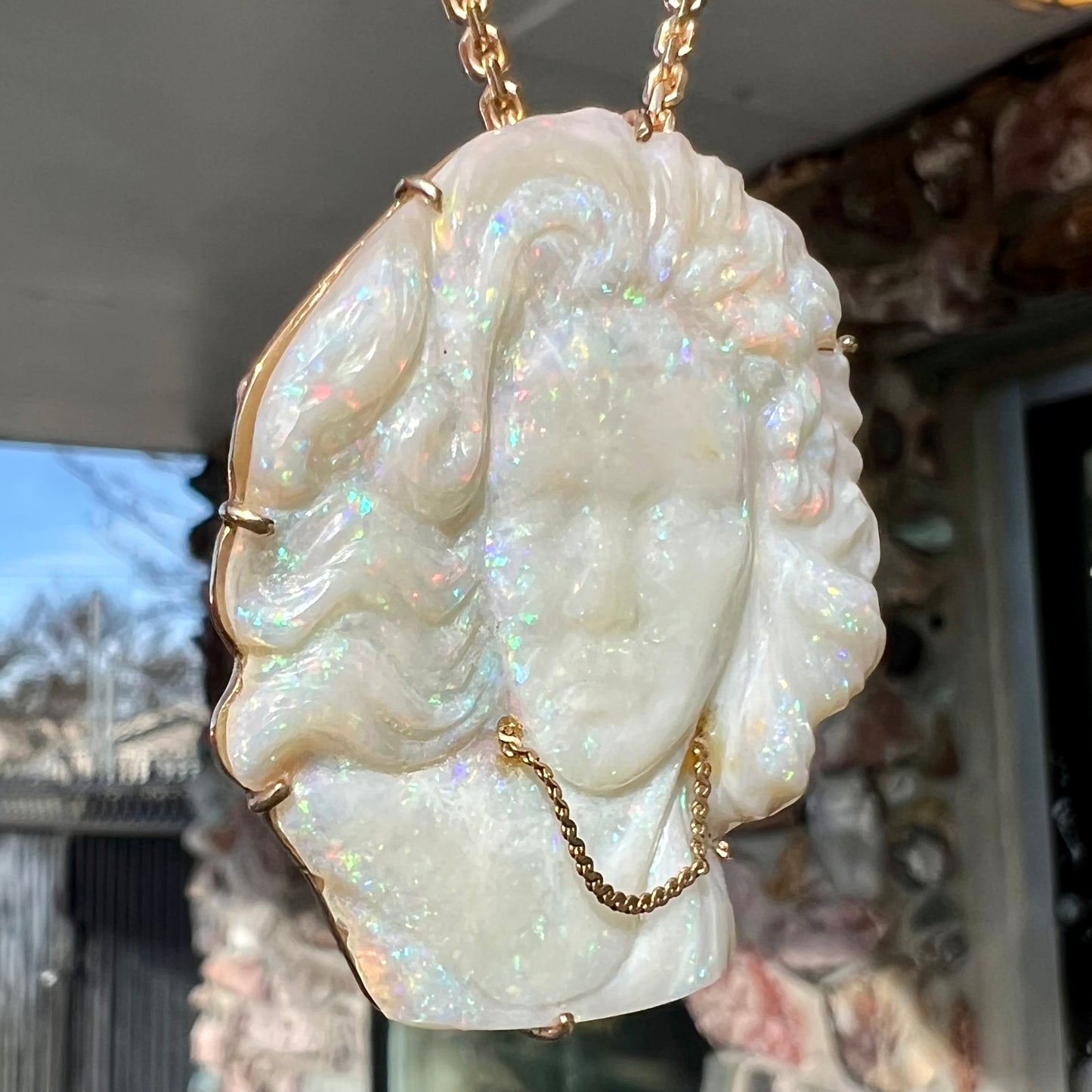 A cameo necklace carved by white crystal opal and held with gold prongs. The cameo is wearing a gold chain.