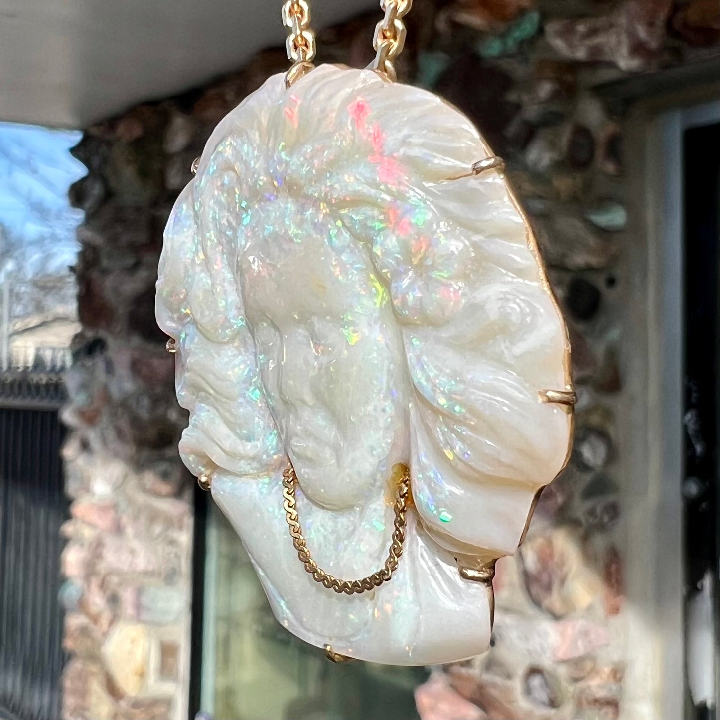 A cameo necklace carved by white crystal opal and held with gold prongs. The cameo is wearing a gold chain.