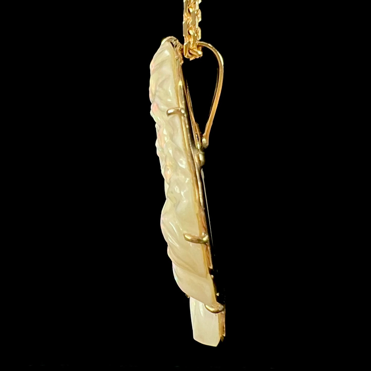 A cameo necklace carved by white crystal opal and held with gold prongs. The cameo is wearing a gold chain.