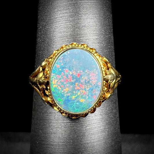 A yellow gold black opal doublet ring with a fleur-de-lis design.