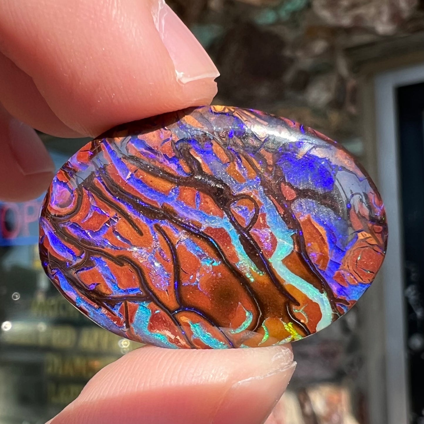 A loose, oval cabochon cut boulder opal from Koroit, Australia. The opal has violet and purple veins.