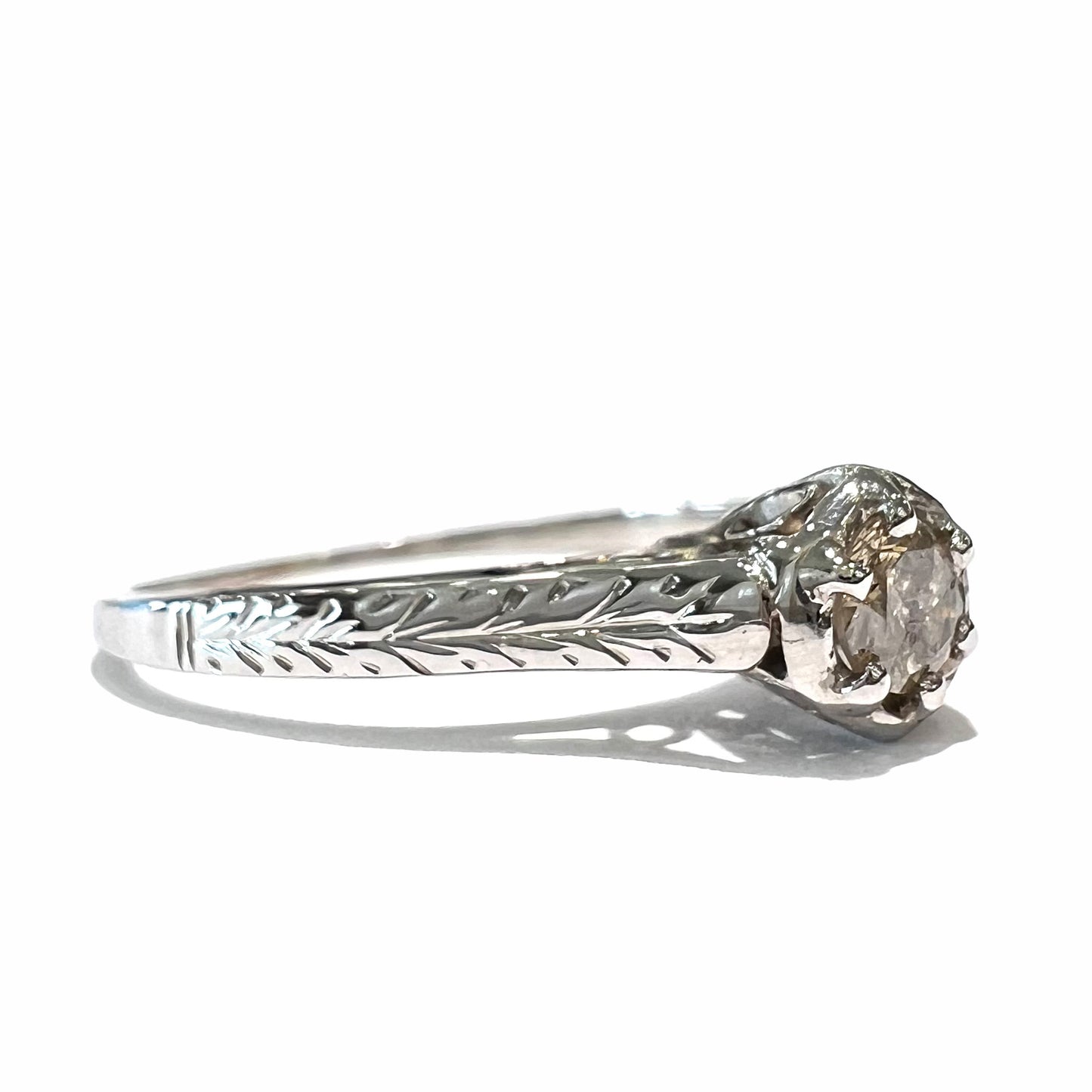 An Art Deco style 18 karat white gold diamond solitaire ring. The ring has scroll work on the side of the shank.
