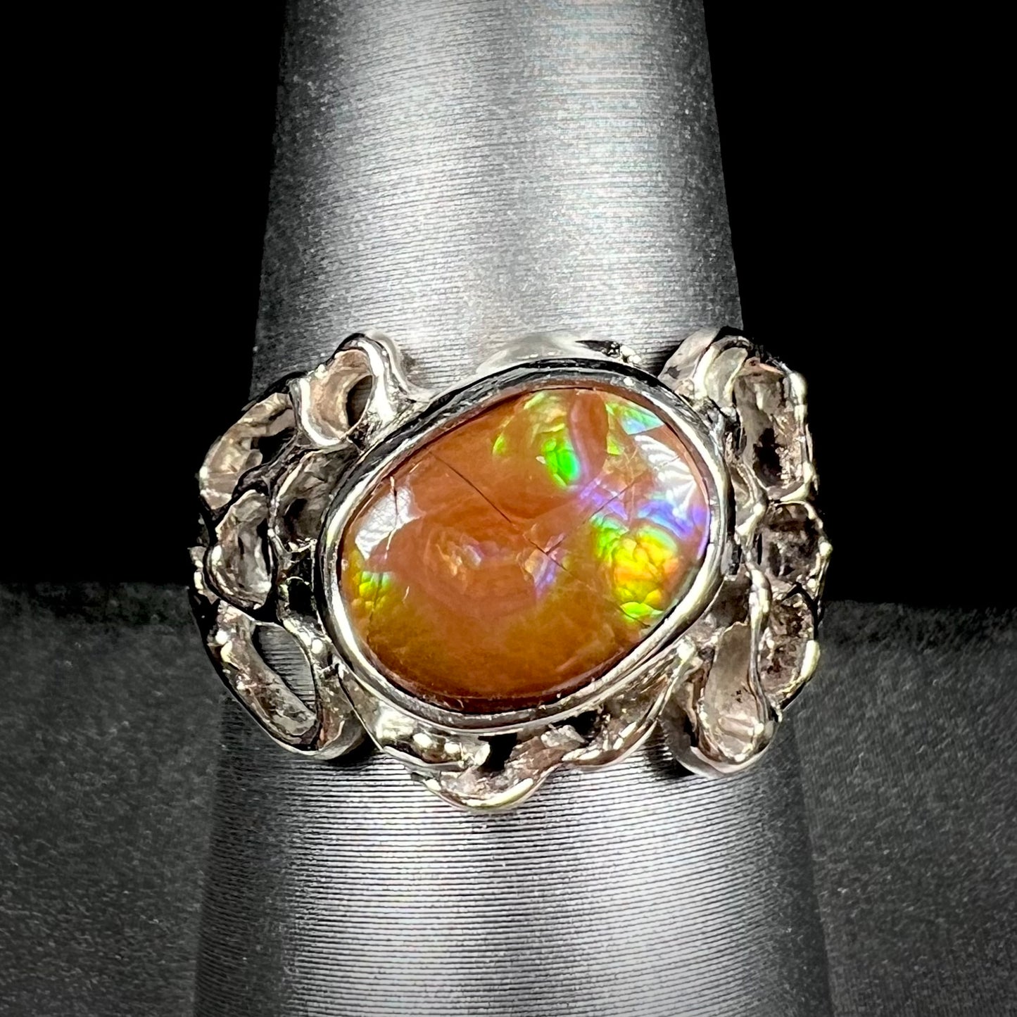 An organic-style white gold men's ring, bezel set with an oval cut Mexican fire agate stone.  The stone is green and purple.