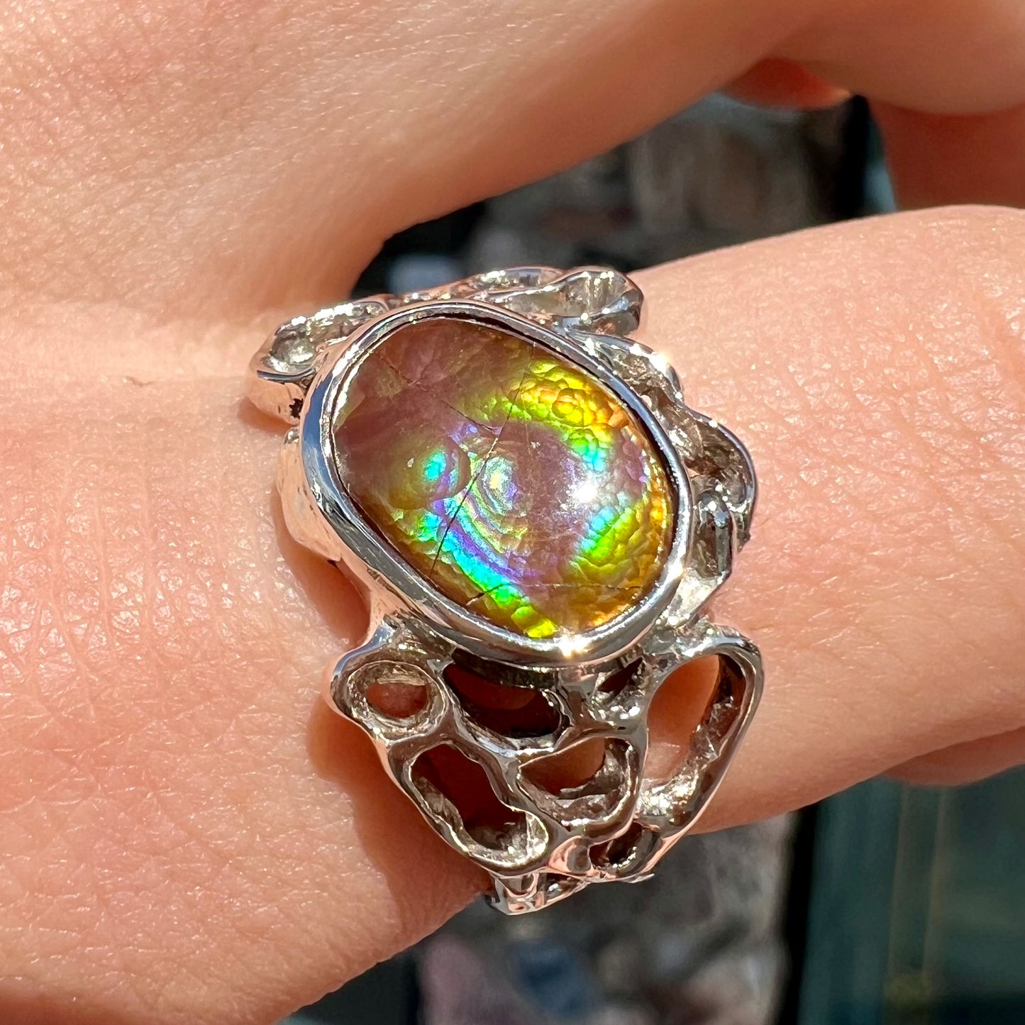 An organic-style white gold men's ring, bezel set with an oval cut Mexican fire agate stone.  The stone is green and purple.