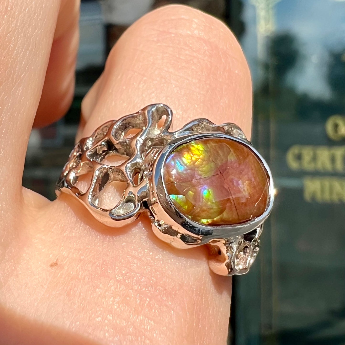 An organic-style white gold men's ring, bezel set with an oval cut Mexican fire agate stone.  The stone is green and purple.