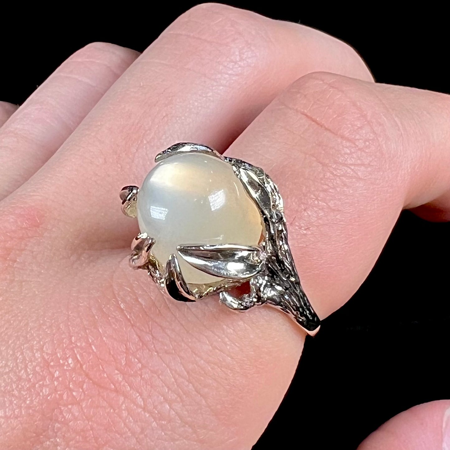 A ladies' organic style white gold moonstone ring. The moonstone shows white adularescence on a creamy white body color. Prongs resemble leaves holding the stone.