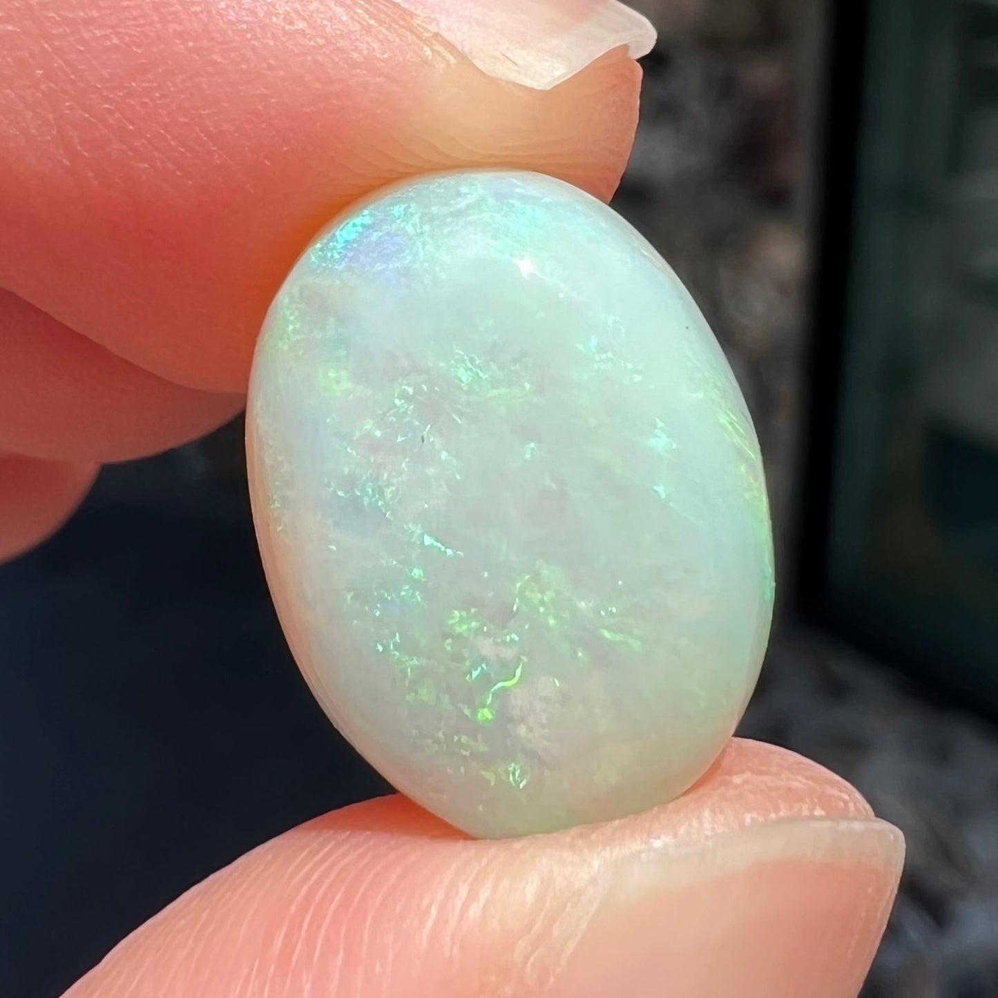 An oval cabochon cut white opal stone from Coober Pedy, Australia. The opal has subtle colors of green and blue.