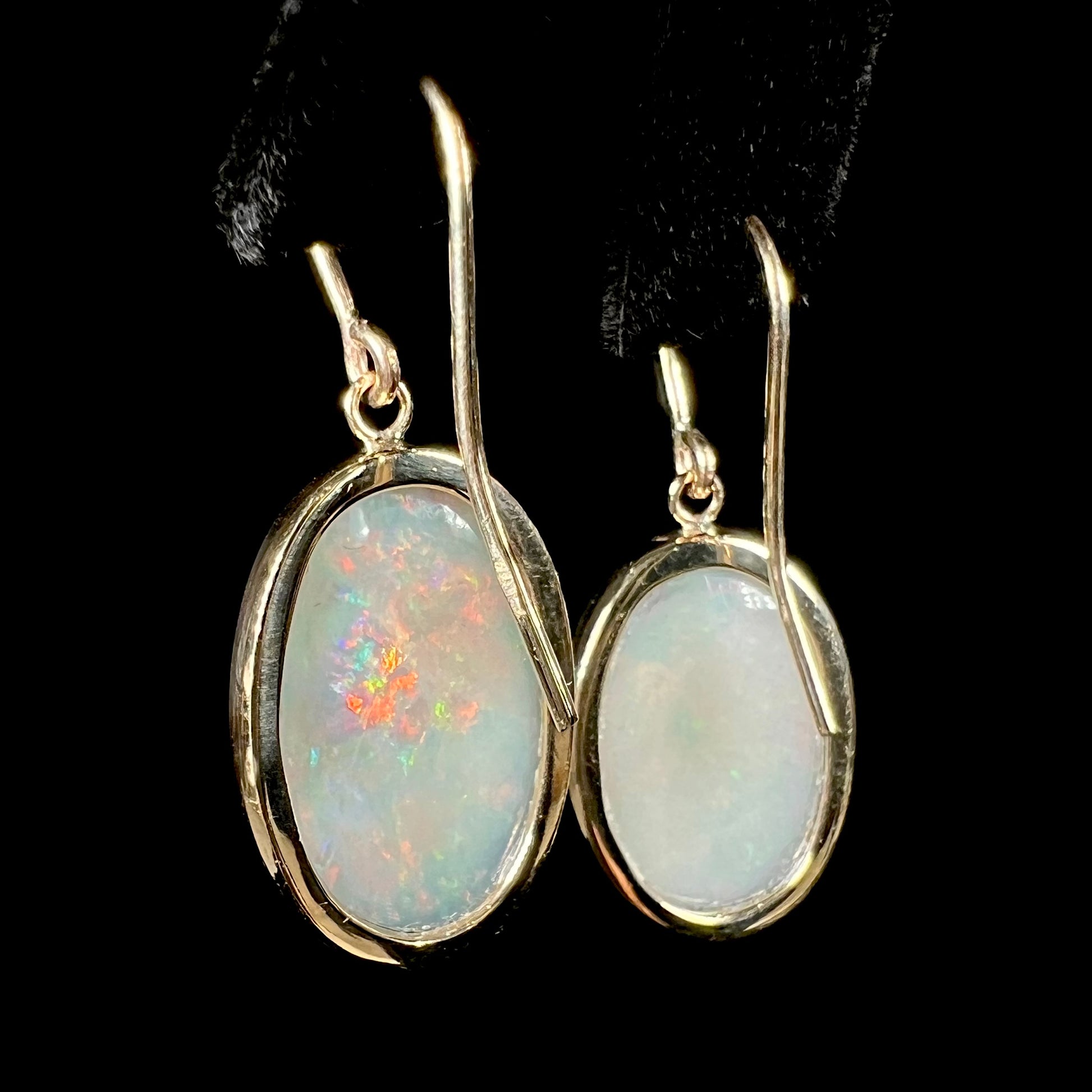 A pair of yellow gold earrings bezel set with oval cabochon cut natural opal stones.