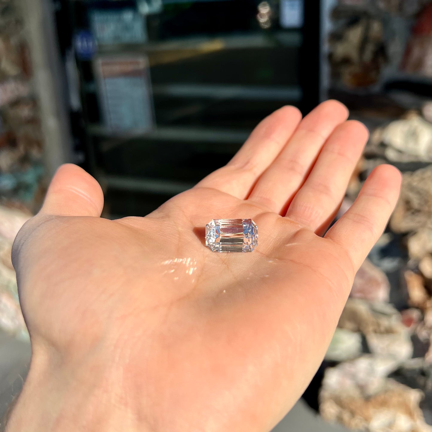A loose, emerald cut topaz gemstone from Russia. The stone is a faint pinkish white color.