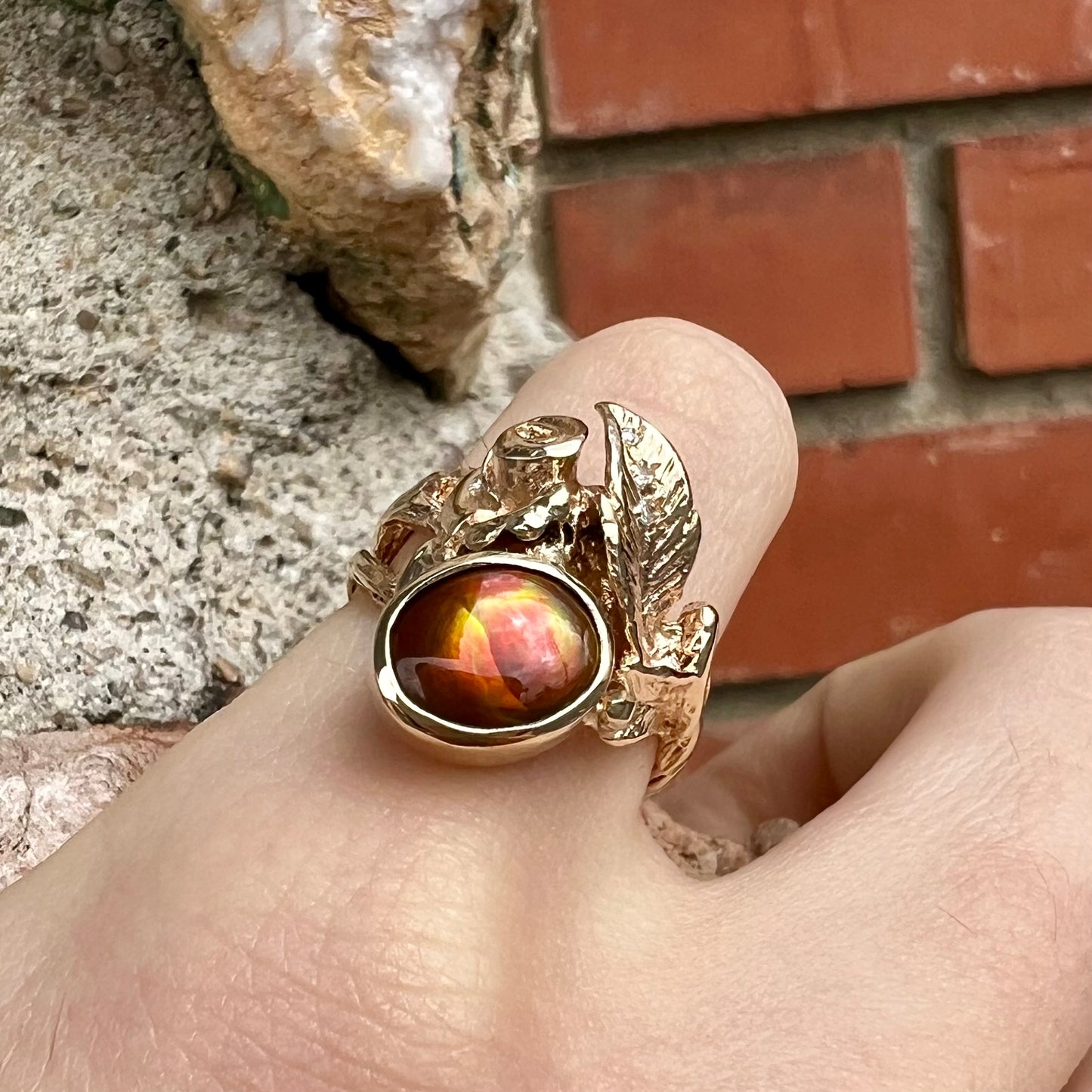 A ladies' yellow gold flower style ring set with an oval cabochon cut fire agate and diamond accents.