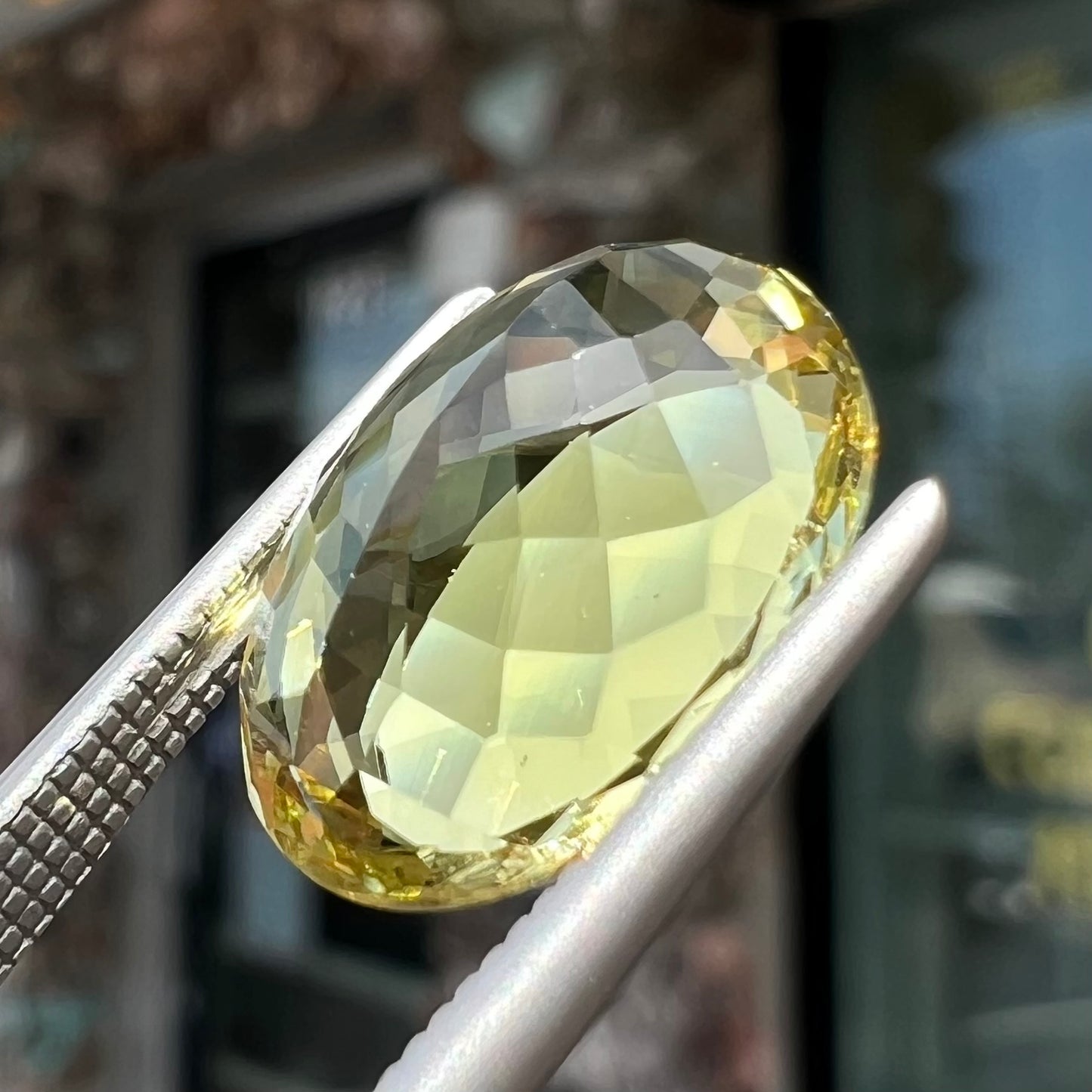 A faceted oval cut golden beryl gemstone. The stone is a greenish light yellow.