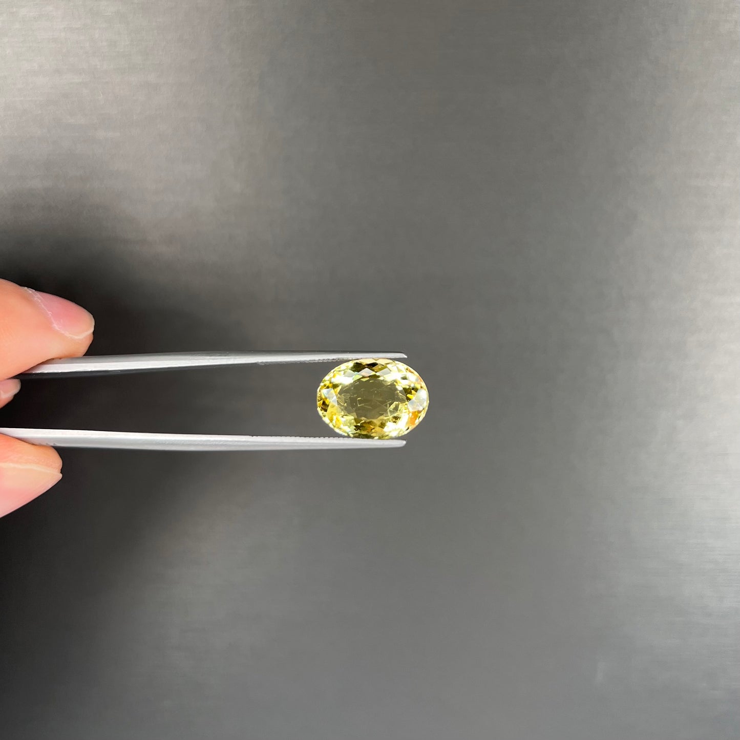 A faceted oval cut golden beryl gemstone. The stone is a greenish light yellow.