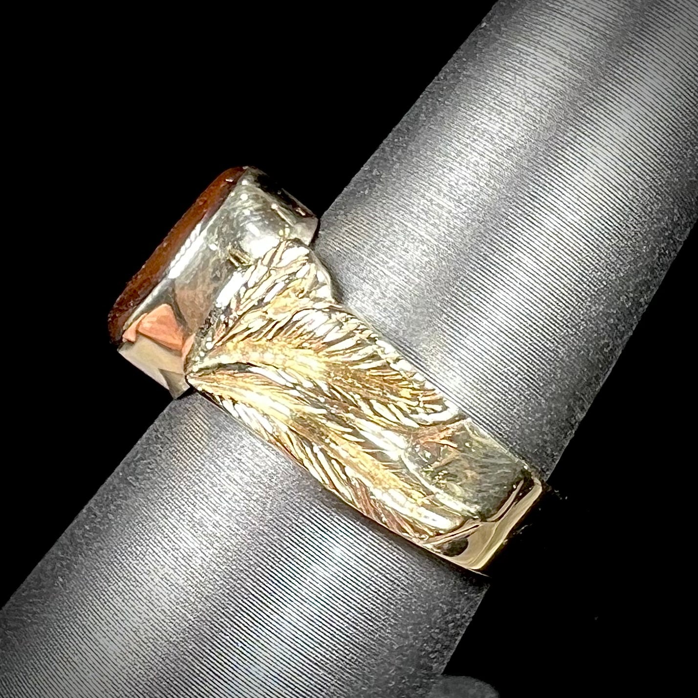 A unisex oval cabochon cut fire agate ring cast in yellow gold. The stone flashes green and red colors.