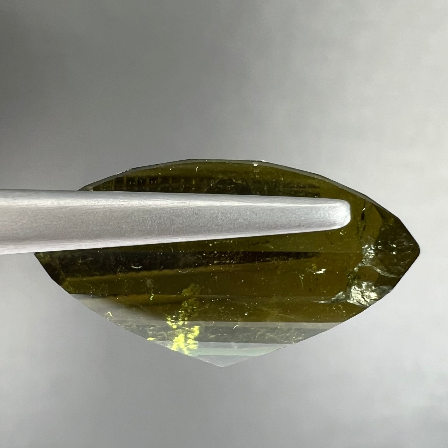 A rectangular step-cut yellowish green tourmaline gemstone.