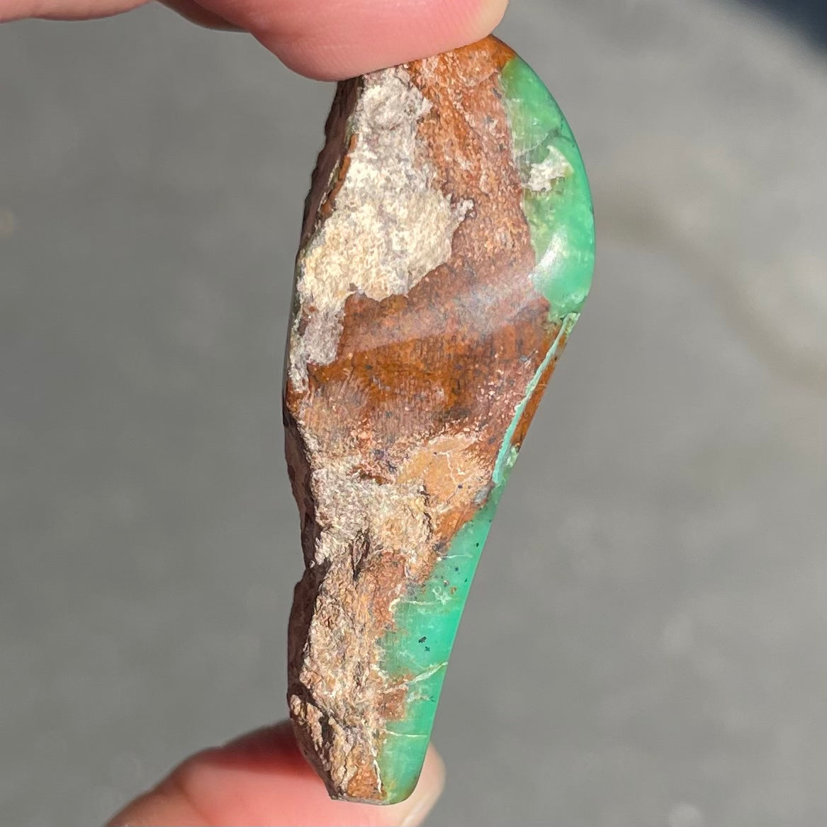 A polished green chrysoprase stone with brown matrix inclusions.