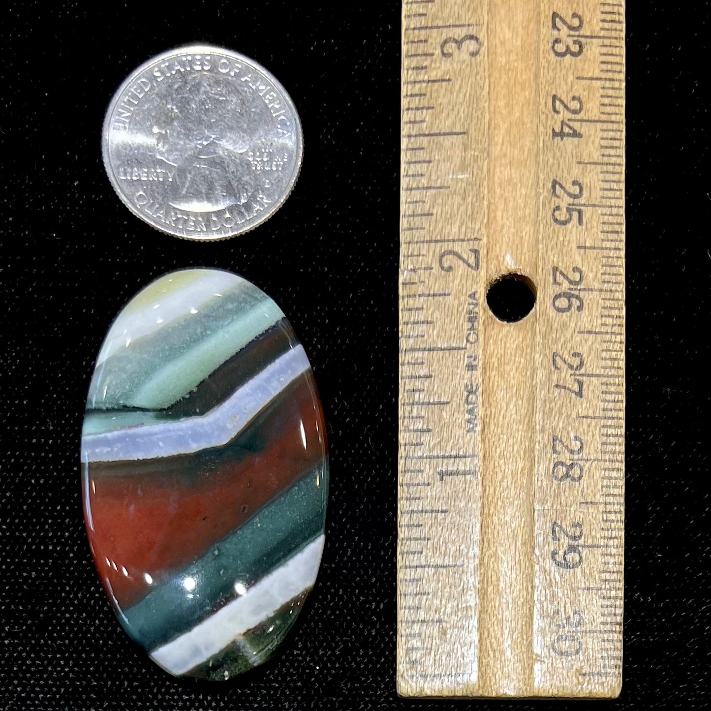 Loose Arizona agate cabochon for sale set on white background. Stone is striped with red, green, and white.